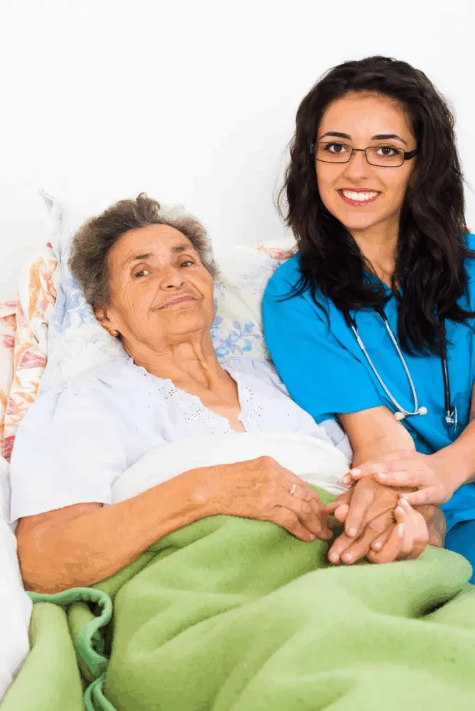 Personal de salud con uniforme azul y estetoscopio sonríe junto a una adulta mayor que descansa en cama