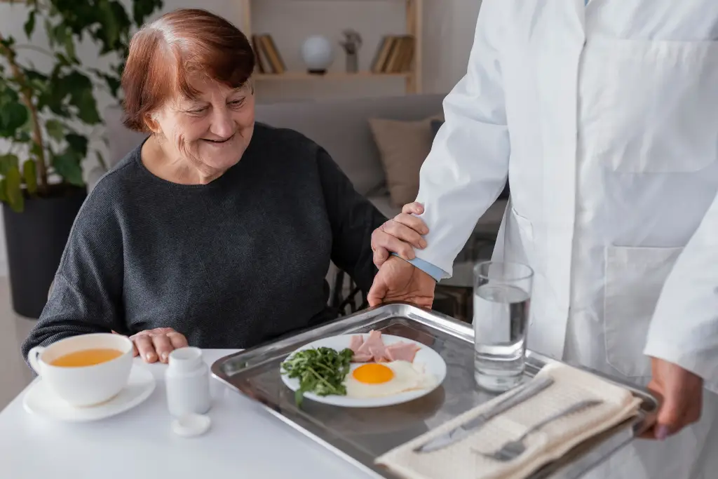 Personal de la residencia sirve una bandeja con un desayuno nutritivo a una adulta mayor sonriente