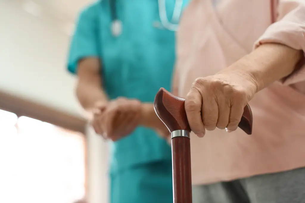 Primer plano de la mano de un residente apoyada en un bastón, recibiendo asistencia del personal de kinesiología