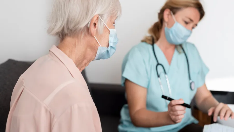 Personal de salud de El Roble Residencia, usando mascarilla, realiza una consulta médica a una residente adulta mayor
